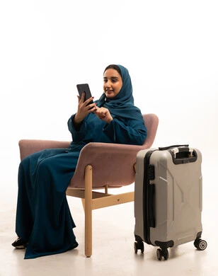 امرأة إماراتية بالعباءة تنتظر مع حقيبة سفر وهاتف