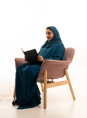 امرأة سعودية بالعباءة تقرأ كتاباً في الاستوديو