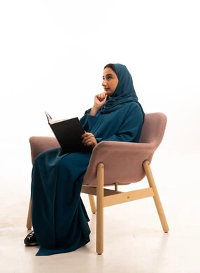 امرأة سعودية بالعباءة تقرأ كتاباً على كرسي عصري