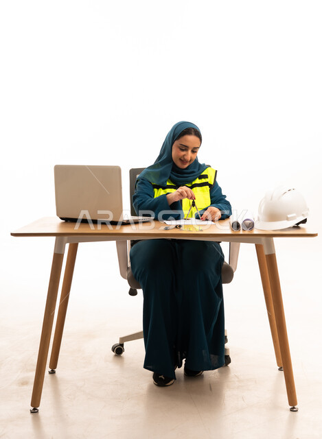 مهندسة سعودية تعمل على المكتب مع أدوات السلامة