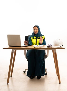 مهندسة سعودية تجلس في مكتب عمل مرتدية سترة سلامة