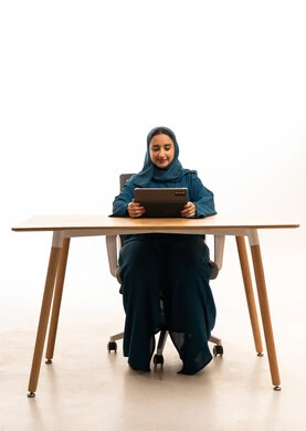 امرأة إماراتية بالعباءة تستخدم جهاز لوحي على المكتب