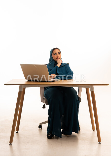 امرأة عربية تفكر خلف مكتب العمل مع لابتوب في استوديو