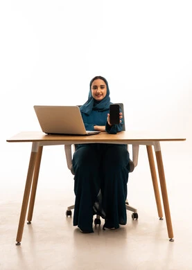 امرأة سعودية مع كمبيوتر محمول وهاتف ذكي في المكتب