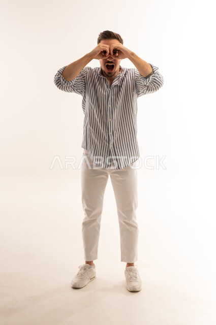 شاب سعودي يقلد شكل المنظار بيديه بخلفية بيضاء