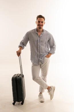 رجل سعودي مبتسم يقف مع حقيبة سفر على خلفية بيضاء