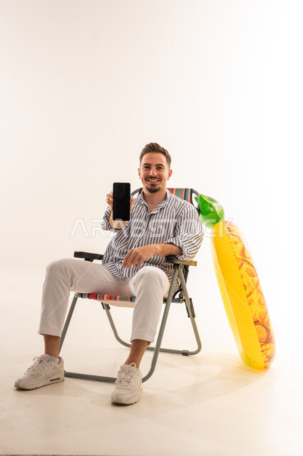 رجل سعودي على كرسي شاطئ يعرض شاشة جوال