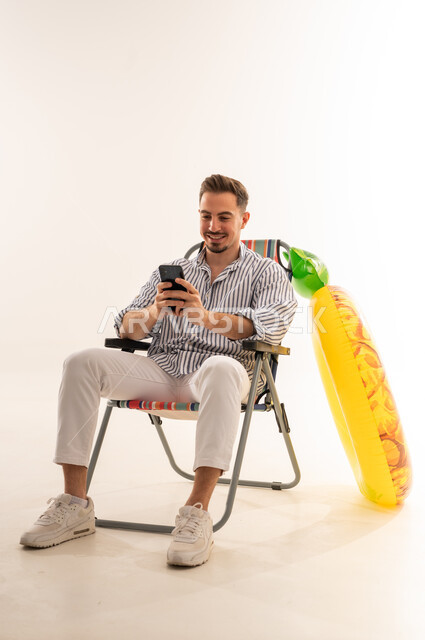 رجل سعودي يحمل هاتفاً ذكياً مع عوامة مسبح أناناس