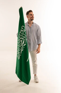 رجل سعودي يمسك علم المملكة العربية السعودية بخلفية بيضاء