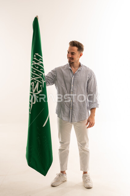 رجل سعودي يحمل علم المملكة العربية السعودية بخلفية بيضاء
