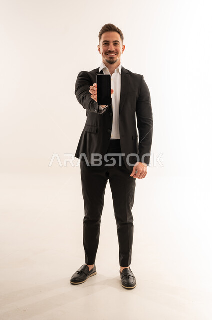 رجل أعمال سعودي يمسك هاتف ذكي بخلفية بيضاء