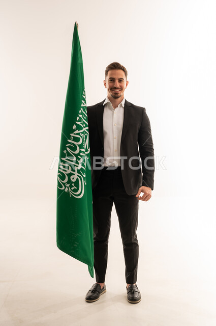 رجل سعودي ببدلة رسمية يحمل علم المملكة العربية السعودية