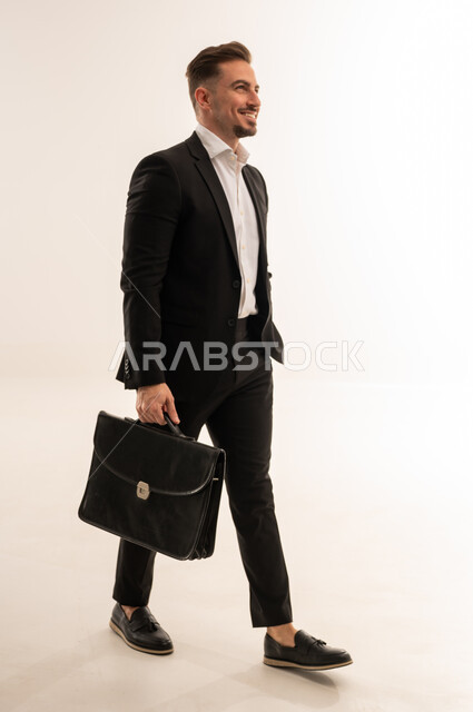رجل أعمال سعودي يمشي مع حقيبة ببدلة رسمية سوداء