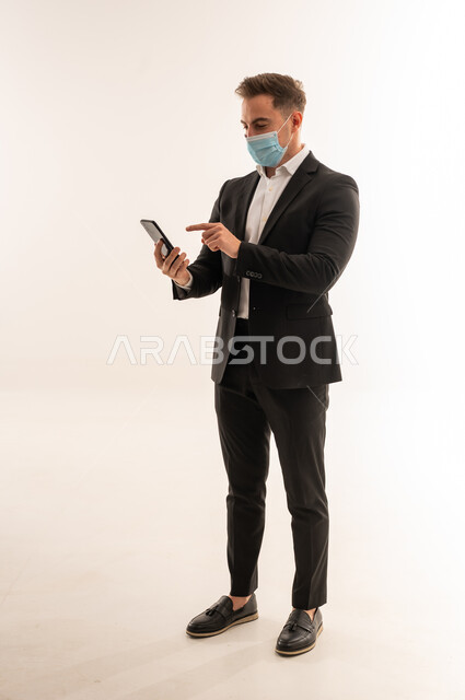رجل أعمال سعودي ببدلة وكمامة يستخدم الهاتف الذكي