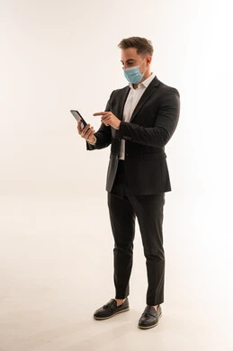 رجل أعمال سعودي ببدلة وكمامة يستخدم الهاتف الذكي