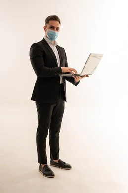 رجل أعمال سعودي يرتدي بدلة رسمية وكمامة طبية مع حاسوب محمول