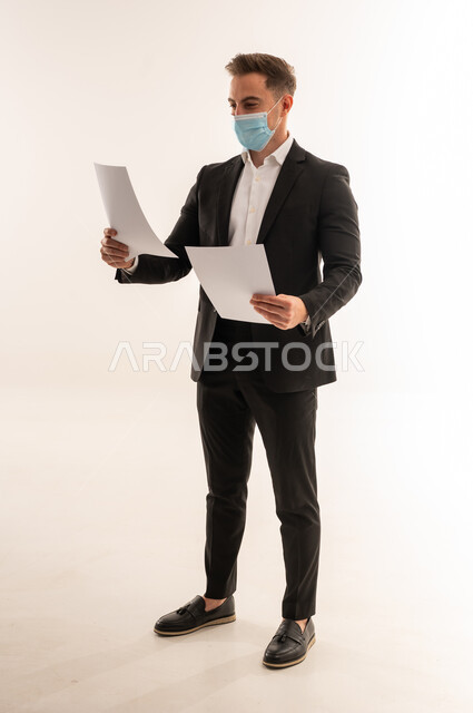 رجل أعمال سعودي يرتدي كمامة ويمسك أوراقاً