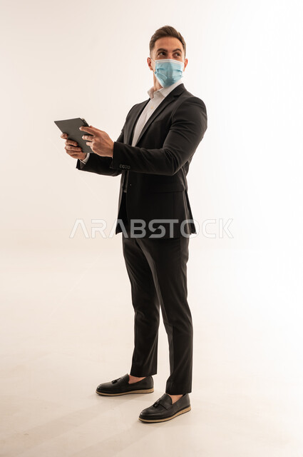 Saudi Businessman in Suit Wearing Mask Holding Tablet