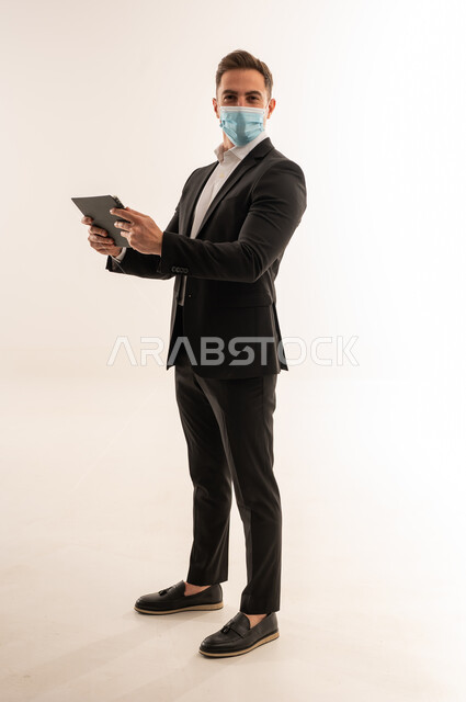 رجل أعمال سعودي يرتدي كمامة مع جهاز لوحي