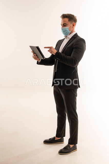 رجل أعمال سعودي يستخدم جهاز لوحي مع كمامة طبية