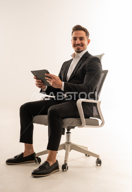 رجل أعمال سعودي بجهاز لوحي على كرسي مكتب