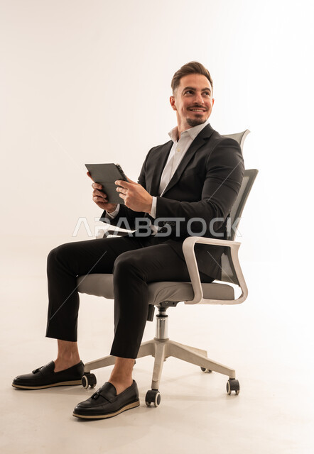 رجل أعمال سعودي يجلس مع تابلت بخلفية بيضاء