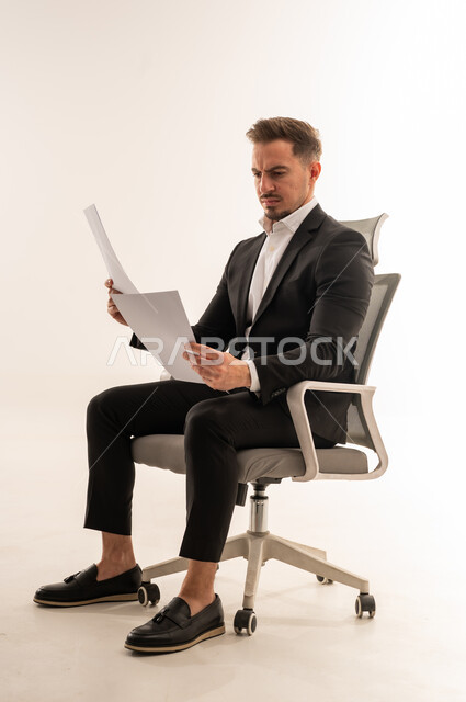 رجل أعمال سعودي يراجع مستندات على كرسي مكتب