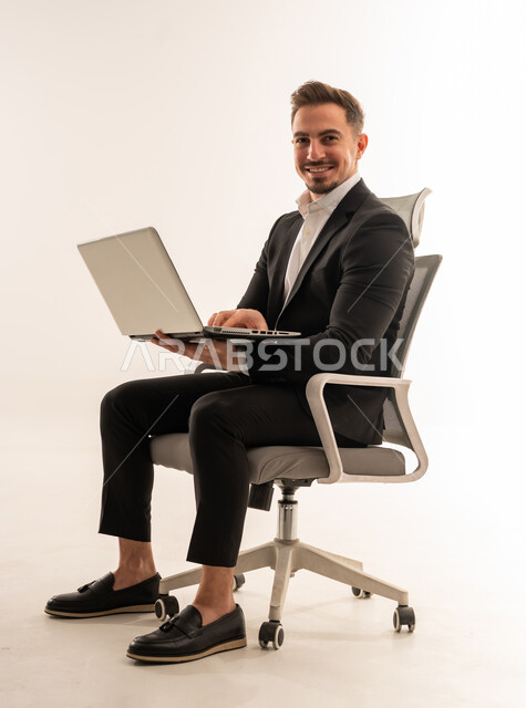رجل أعمال سعودي يجلس مع كمبيوتر محمول بخلفية بيضاء