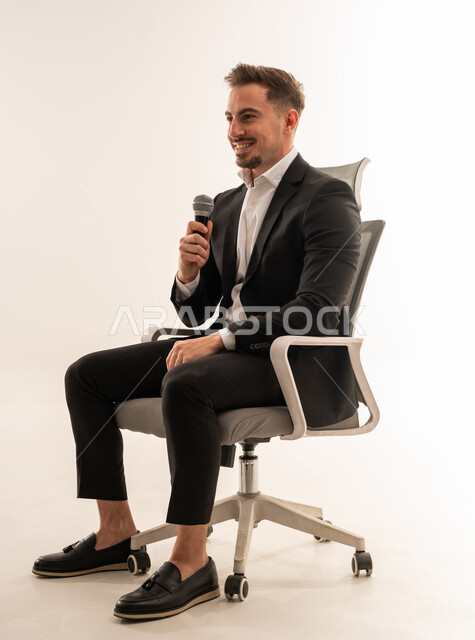 رجل أعمال سعودي يتحدث بميكروفون على كرسي مكتب