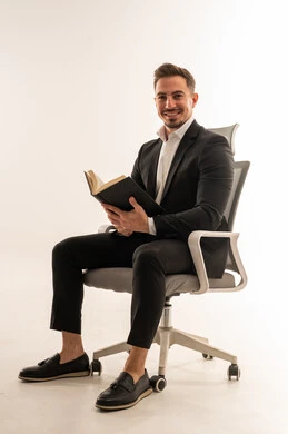 رجل أعمال سعودي يرتدي بدلة يقرأ كتاباً على كرسي