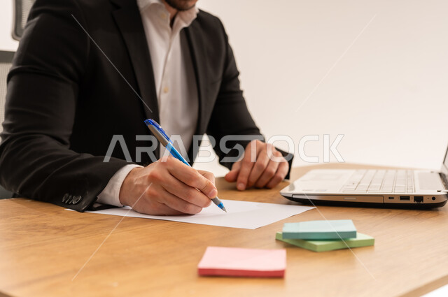 رجل أعمال سعودي يكتب على مكتب عمل مع لابتوب