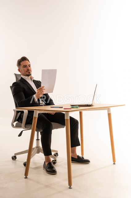 رجل أعمال سعودي يقرأ وثيقة على مكتب مع لابتوب