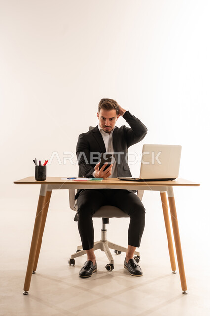 رجل أعمال سعودي جالس على مكتبه مع هاتف ذكي