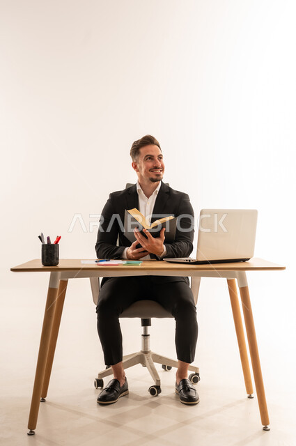 رجل أعمال سعودي يقرأ كتاباً على مكتب بخلفية بيضاء