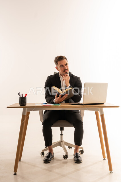 رجل أعمال سعودي على مكتب العمل يفكر مع كتاب