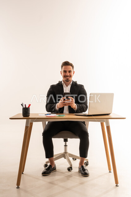 رجل أعمال سعودي على مكتب العمل مع هاتف ذكي
