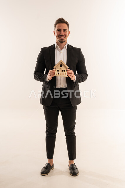 رجل أعمال سعودي يمسك نموذج منزل على خلفية بيضاء
