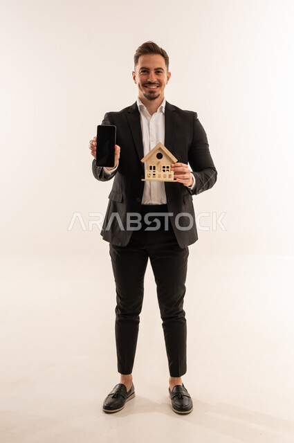 رجل أعمال سعودي يحمل نموذج منزل وهاتف ذكي