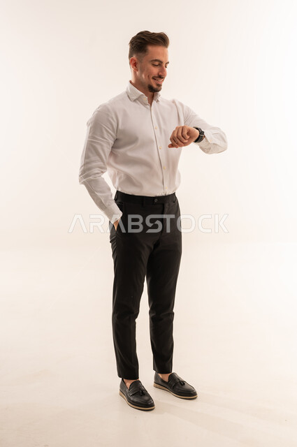 رجل أعمال سعودي يتفقد ساعة يده بخلفية بيضاء