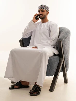 رجل عماني بالدشداشة التقليدية يتحدث عبر الهاتف الذكي