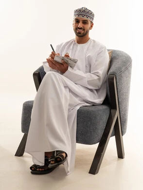 رجل عماني بالزي التقليدي يكتب في دفتر