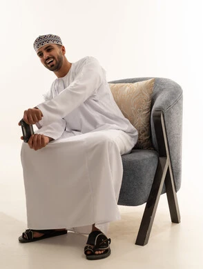 رجل عماني بالدشداشة يمسك جهاز تحكم ألعاب