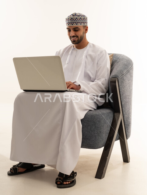 رجل عماني يستخدم حاسوب محمول على كرسي في استوديو