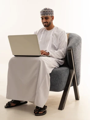 رجل عماني يستخدم حاسوب محمول على كرسي في استوديو