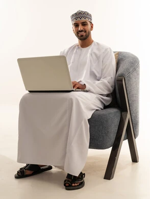 رجل عُماني بالزي التقليدي يستخدم جهاز كمبيوتر محمول