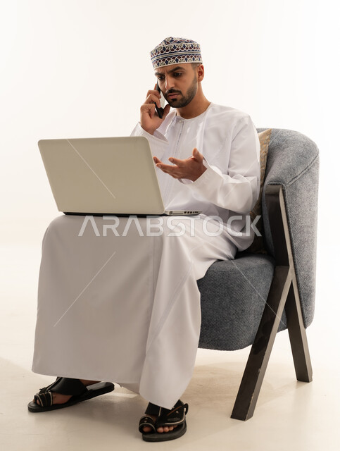 رجل عماني بالزي التقليدي يستخدم المحمول والكمبيوتر