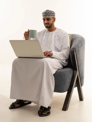 رجل عماني يعمل على اللابتوب باللباس التقليدي