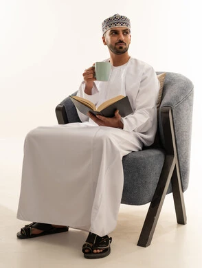 رجل عماني بالزي التقليدي يقرأ كتابا مع القهوة