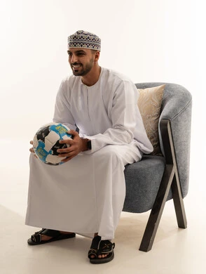 رجل عماني بالزي التقليدي يمسك كرة قدم