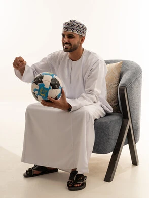 رجل عُماني بالزي التقليدي يحمل كرة قدم